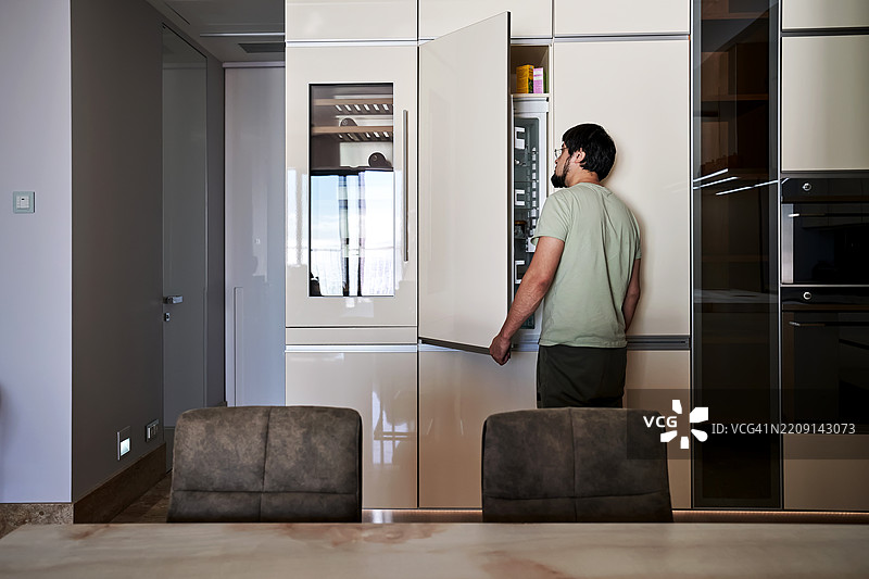 一位中年男子打开冰箱，正在寻找食物。图片素材
