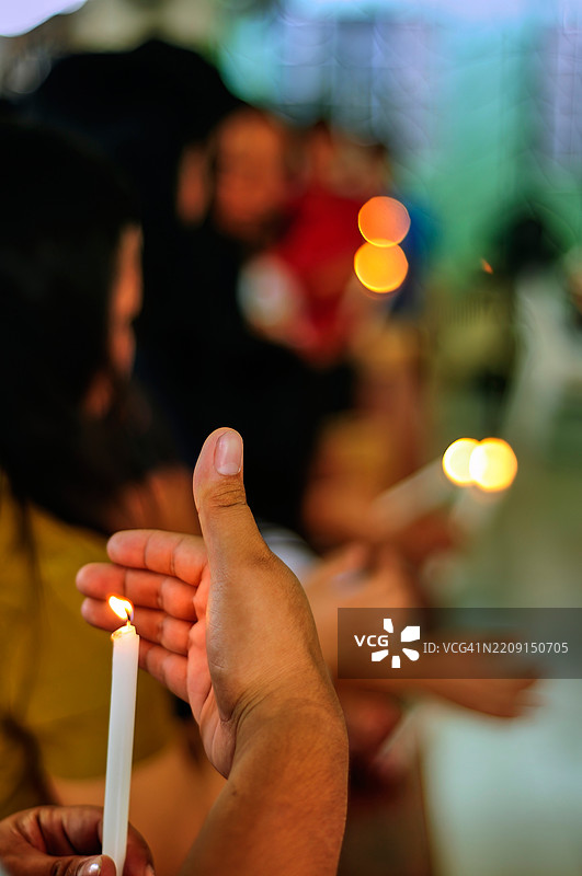 一个人手握着点燃的蜡烛在弥撒中。图片素材