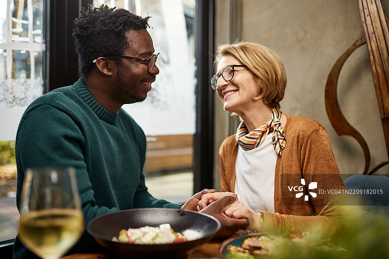 相爱的一对年龄差异的情侣在餐厅里牵手对视。图片素材