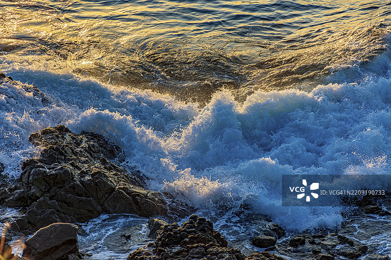 在巴西南美洲的萨尔瓦多，巴伊亚，日落时分，海浪在岩石上翻腾起泡沫。图片素材