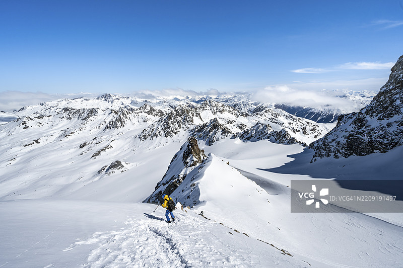 冬季登山者手持冰镐和冰爪，攀登陡峭的雪地，前往Piz Kesch或Piz d'Es-cha，远眺Vadret da Porchabella冰川的山脉全景，阿尔布拉阿尔卑斯山，瑞士拉赫蒂安阿尔卑斯山，格劳宾登州，瑞士东部，欧洲图片素材