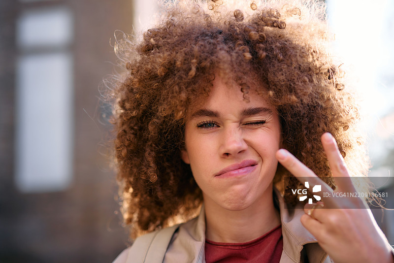 年轻学生在户外眨眼并做出和平手势图片素材