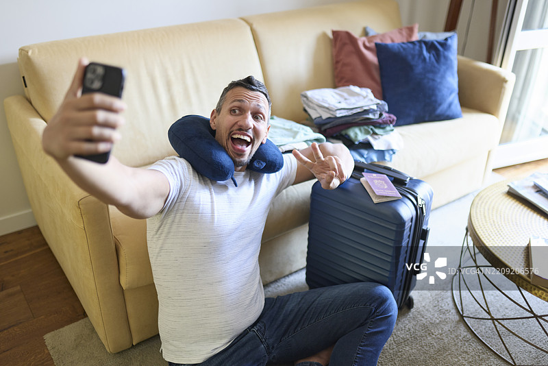 兴奋的男人在旅行前与行李箱和旅行必需品自拍图片素材