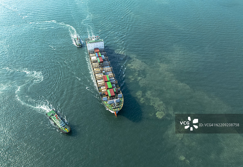 航拍视角，拖船正在将集装箱船推入港口。商业贸易物流和国际运输，集装箱货船的进出口。图片素材