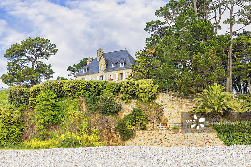 夏季时，位于法国布列塔尼克罗宗半岛摩尔加特的海滩旁，绿意盎然的山坡上的房子图片素材
