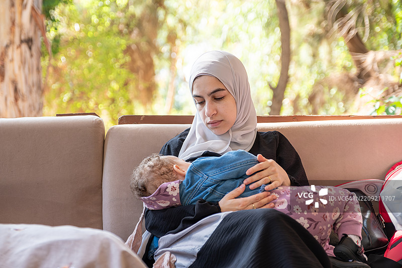 一幅宁静的画面，温柔的母亲在户外的沙发上抱着她的宝宝。图片素材