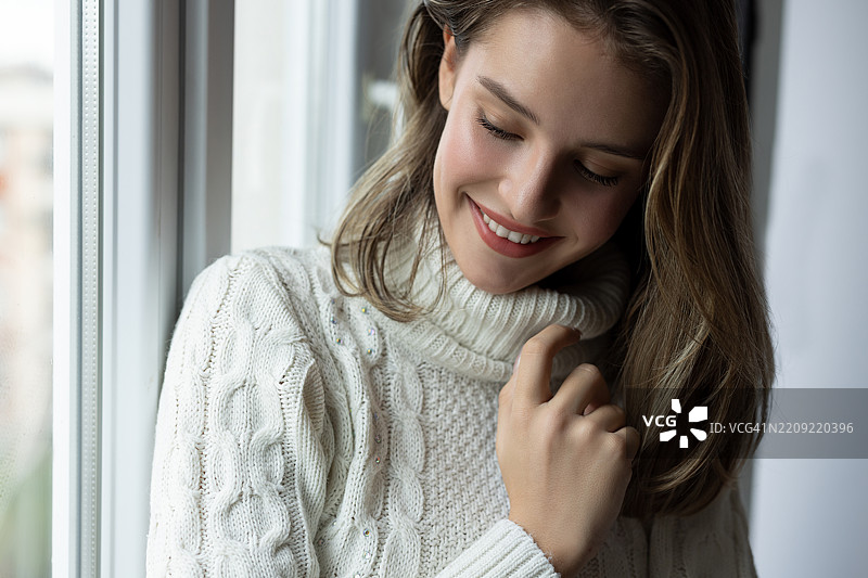 美丽的女人站在窗前，感到温馨舒适图片素材