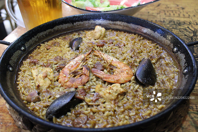 一张传统西班牙海鲜烩饭的特写照片，盛在黑色的烩饭锅中。图片素材