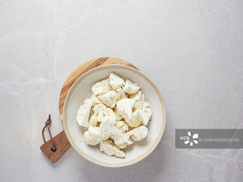 新鲜生花椰菜切成小花朵，放在木砧板上的盘子里，背景是灰色的台面。俯视图，留有空白空间。蔬菜食材准备。图片素材