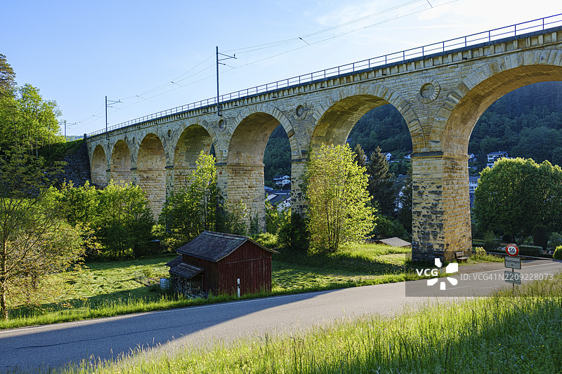 大型石拱桥横跨绿色景观，明亮的天空和一条小路，瑞士巴塞尔地区的瑞姆林根图片素材