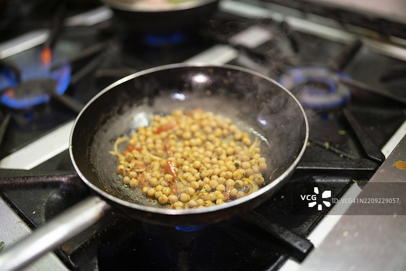 在专业厨房的燃气灶上，鹰嘴豆在慢炖中释放蒸汽，空气中弥漫着诱人的香气，预示着一顿营养丰富且美味的餐点。图片素材