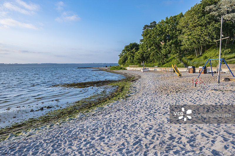 一片沙滩旁有一个游乐场，周围环绕着许多树木，天空晴朗略带云彩，位于德国格吕克斯堡，欧洲图片素材