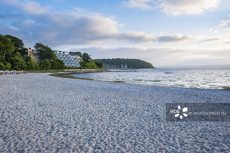 一个安静的沙滩，海景尽收眼底，周围被绿色树木和建筑环绕，天空多云，位于德国格吕克斯堡，欧洲图片素材