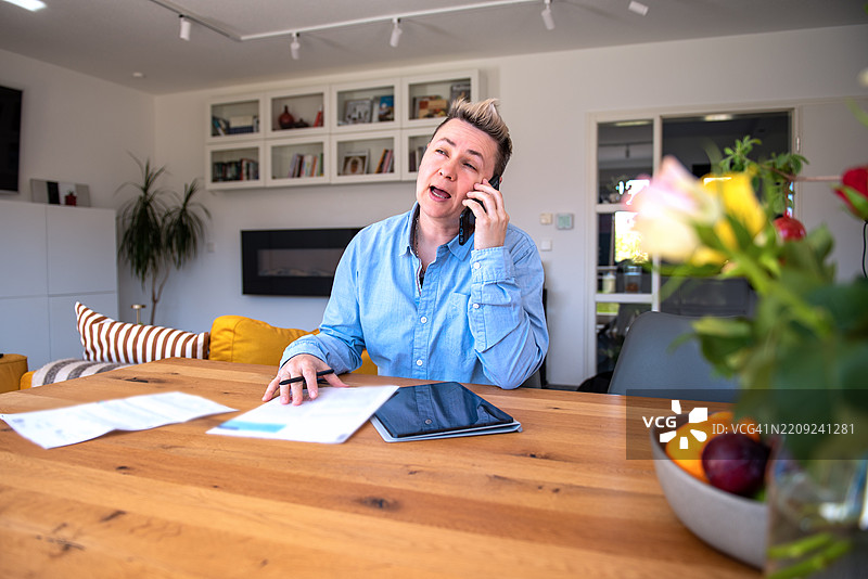 在家办公桌前，因账单而感到沮丧的人正在打电话。图片素材