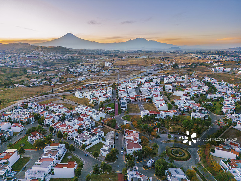 墨西哥普埃布拉的圣克拉拉·奥科尤坎住宅区的航拍，背景是日落时分的波波卡特佩特尔火山和伊萨卡奇瓦特尔火山。图片素材