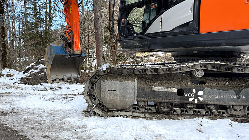 橙色挖掘机在森林中雪地上，带有履带和机械铲斗图片素材
