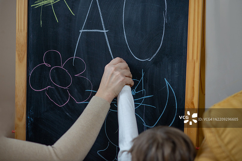 老师在包容性学习活动中帮助小孩（有特殊需要）在黑板上绘画和写字。图片素材