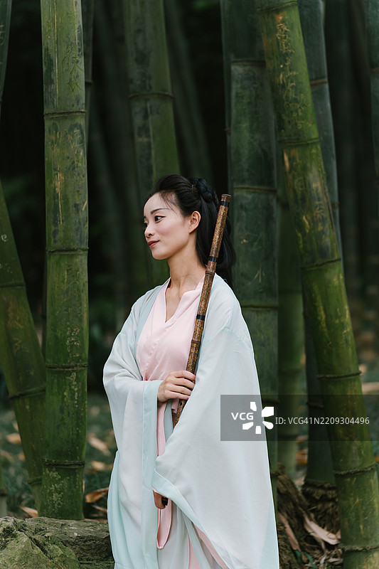 汉服的魅力：穿着汉服的中国女性在竹林中吹笛图片素材