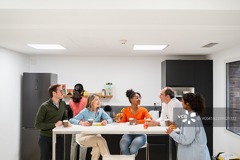 一群多元化的同事在现代办公室厨房里聊天和吃东西，享受咖啡休息时间。图片素材