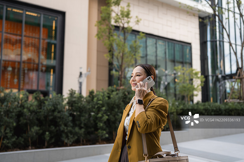 自信的女高管一边走路一边愉快地打电话，穿着高跟鞋。图片素材