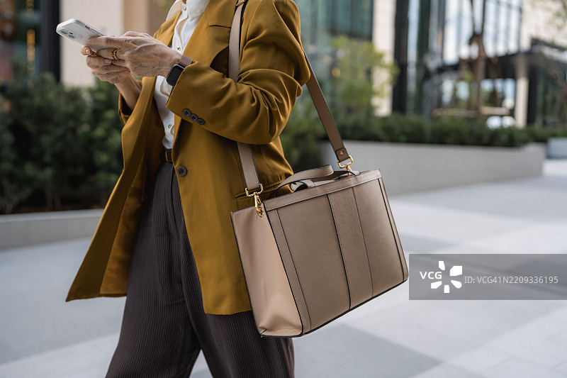 自信的高级女商人愉快地穿着高跟鞋走路时发短信图片素材