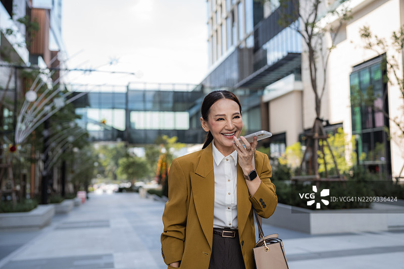 自信的女高管一边走路一边愉快地打电话，穿着高跟鞋。图片素材