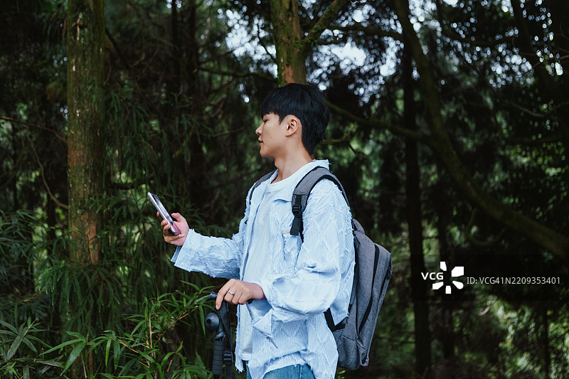 一位年轻的亚洲男子背着背包和登山杖在森林中探险，享受大自然和健康的生活方式。图片素材