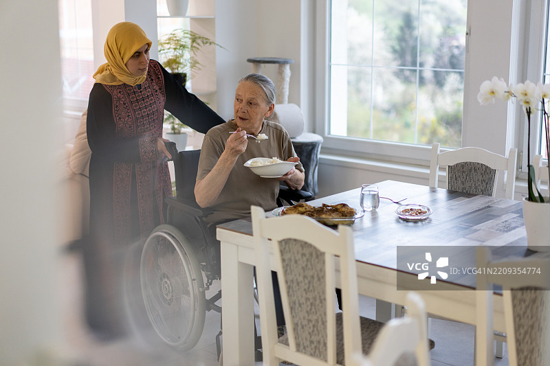 在阳光明媚、温馨的家居环境中，坐在轮椅上的老年女性正在接受照顾图片素材