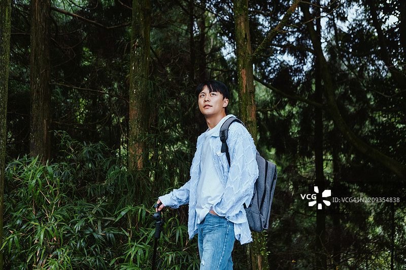 一位年轻的亚洲男子背着背包和登山杖在森林中探险，享受大自然和健康的生活方式。图片素材
