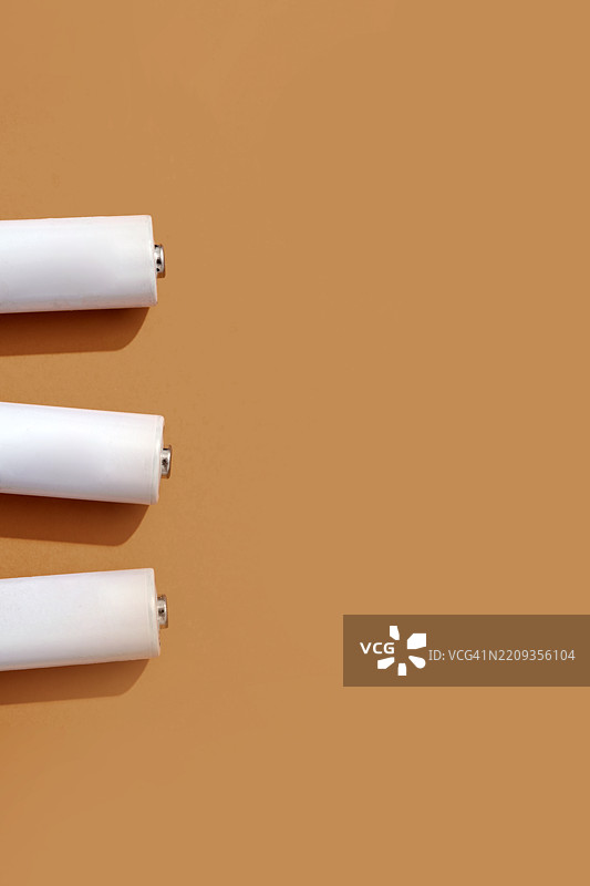 三节白色电池躺在棕色背景上图片素材