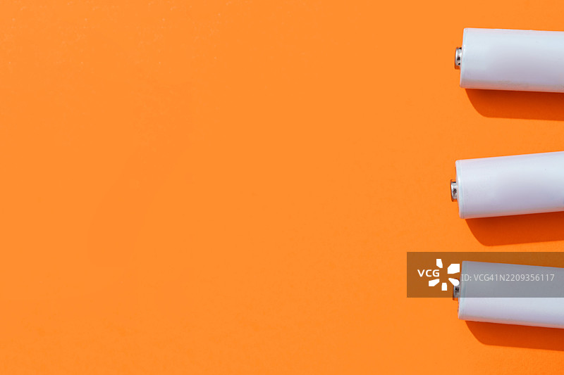 三节电池放在橙色背景上，投射出阴影图片素材