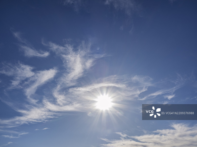 蓝天上有稀薄的高云，阳光照耀在地平线上。图片素材