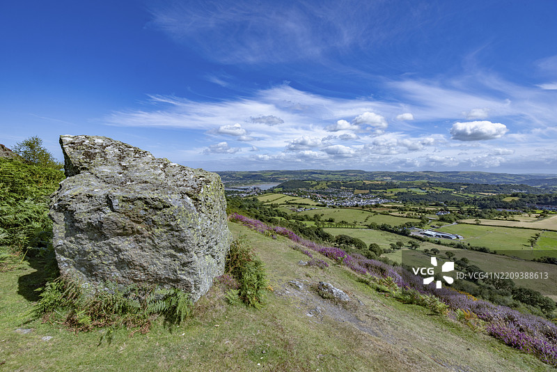 从山上俯瞰康威城堡，古老的城堡遗址被绿色田野和蓝天环绕，前景有一块岩石，位于威尔士的康威，格温内斯郡，欧洲。图片素材