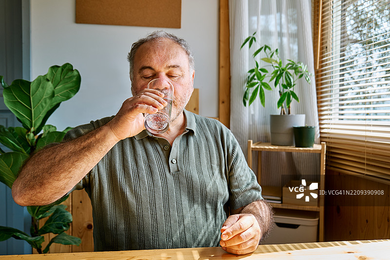 成熟男性在家中早晨喝水，服用维生素药丸和药物。图片素材