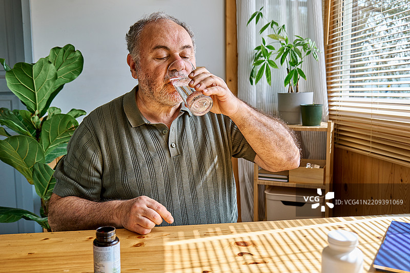 成熟男性在家中早晨喝水，服用维生素药丸和药物。图片素材