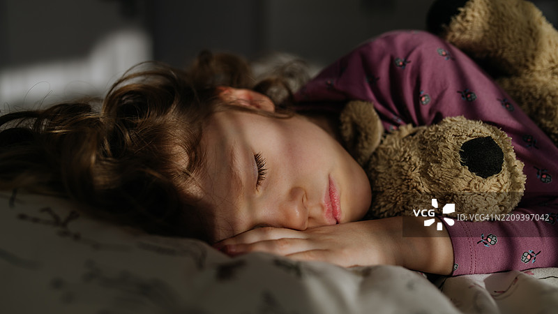 女孩紧紧抱着她的泰迪熊玩具，安静地睡着。图片素材