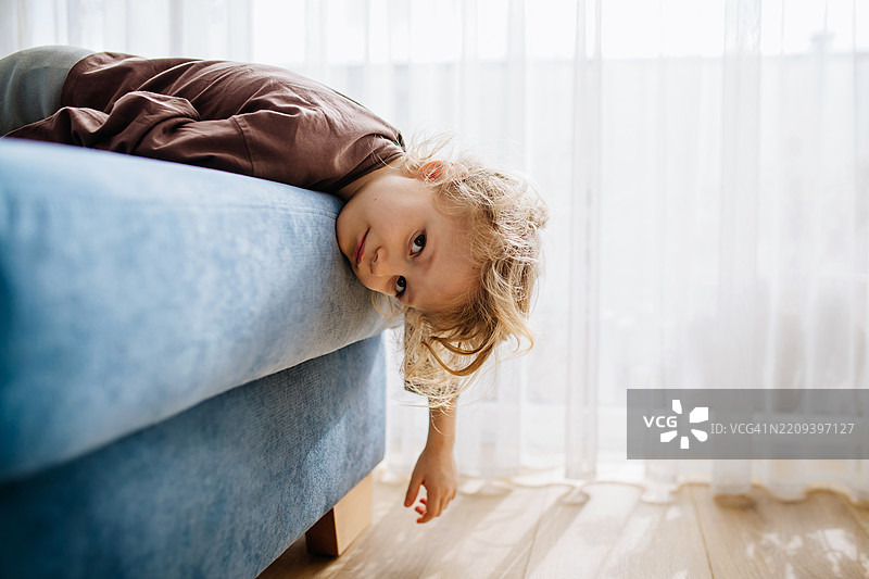 无聊的小女孩躺在沙发上无所事事。图片素材