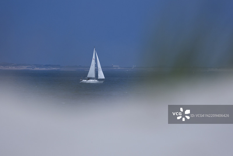 透过沙丘看到一只白色帆船在蓝色海面上，格鲁德，泽兰，荷兰图片素材