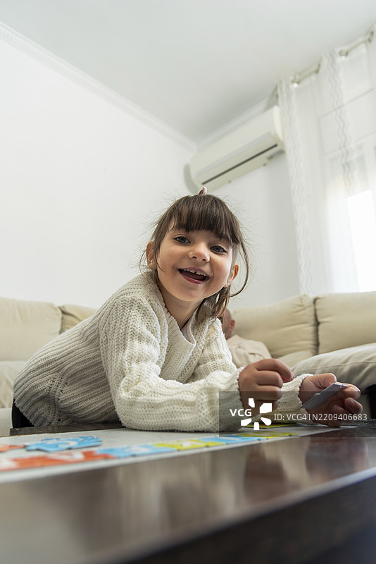 微笑的女孩在咖啡桌上拼装五彩斑斓的拼图，享受在家中富有创意和快乐的休闲时光图片素材