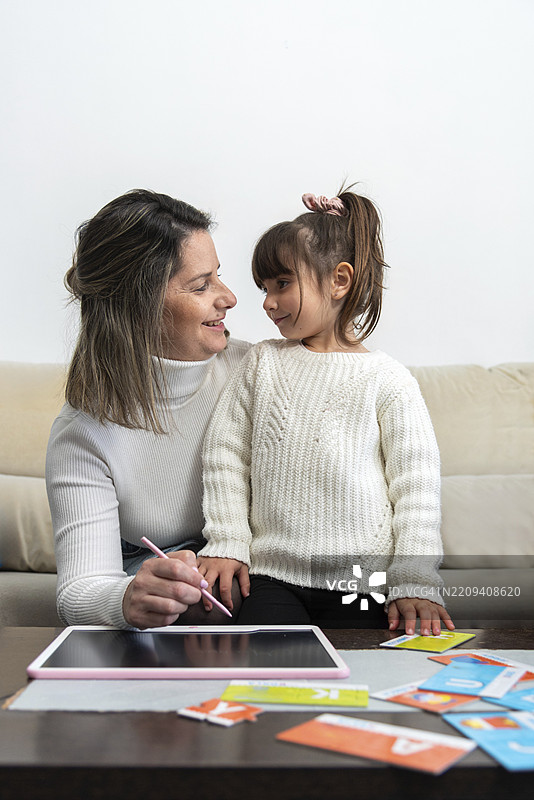 母亲在家帮助女儿进行在线教育，使用平板电脑和字母卡进行互动学习图片素材