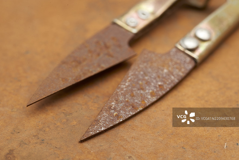 生锈刀刃的老式缝纫剪刀放在风化的皮革上，传达出复古手工工具的逐渐衰退和怀旧的磨损感。图片素材