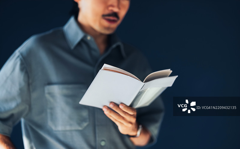 男人在深蓝色背景前阅读一本书图片素材