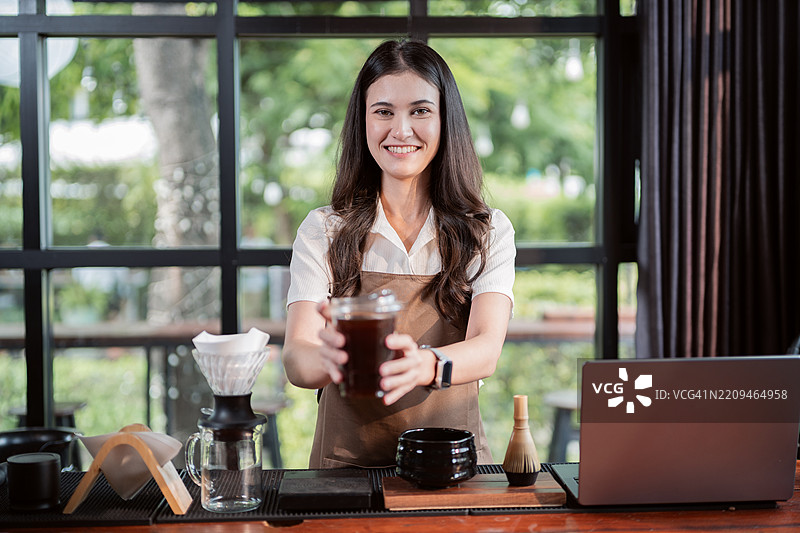 快乐的女咖啡师在咖啡店的柜台上专注于咖啡质量，手中拿着一杯咖啡。图片素材