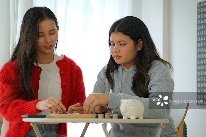 漂亮的女人和朋友在家里数硬币。图片素材