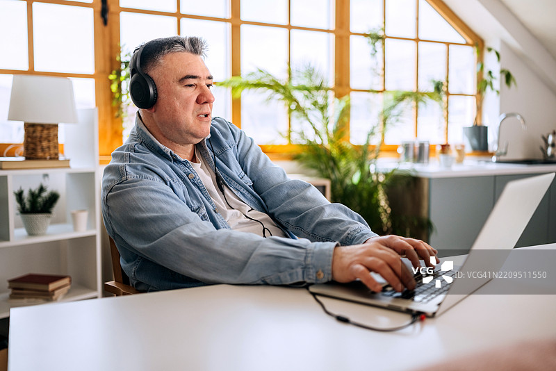 成熟男性在家中使用笔记本电脑并佩戴耳机图片素材