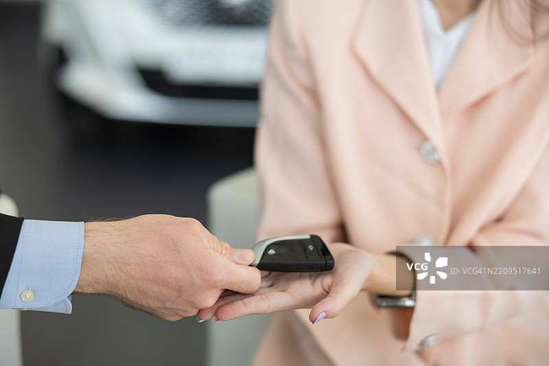 男汽车销售员在现代展厅白天将车钥匙交给开心的顾客，象征着成功的购车、优质的客户服务和车辆交接体验。图片素材