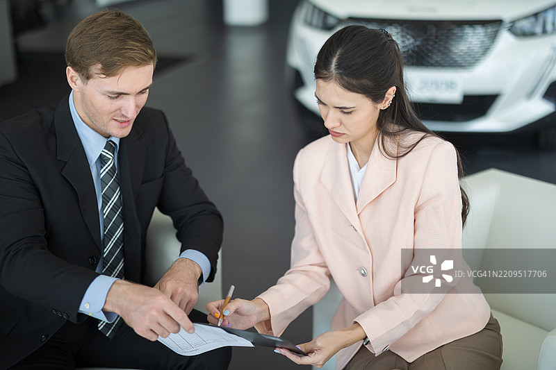 男性汽车销售员在现代汽车展厅内与潜在客户交流，讨论车辆特点和销售选项，进行关于购买新车的商务对话。图片素材