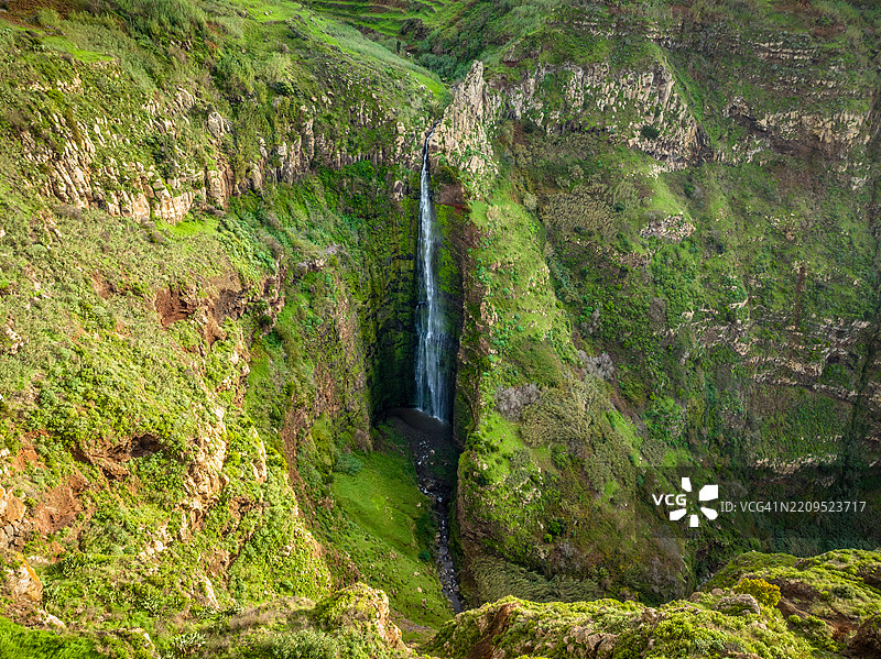 甘卡尔塔丰达瀑布在郁郁葱葱的绿色景观中倾泻而下，戏剧性的空中视角展现了葡萄牙马德拉岛深邃的峡谷，捕捉到原始的自然风光。图片素材