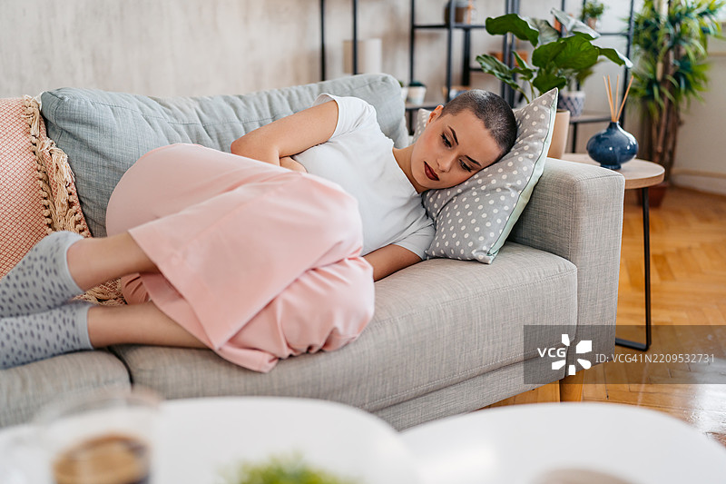 年轻女性在家中因月经疼痛而感到不适，剃短发。图片素材