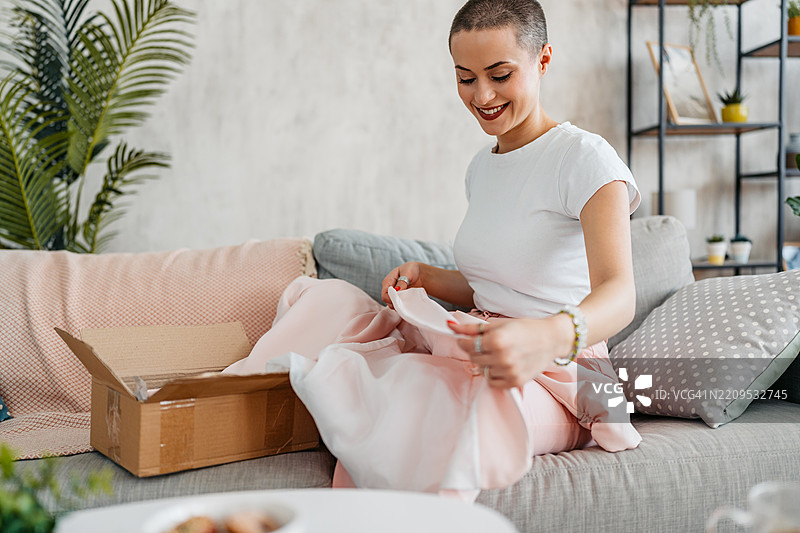 年轻女性剃短发正在拆包裹，里面是她在线订购的新西装外套图片素材